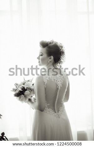 The bride stands with a bouquet at the window