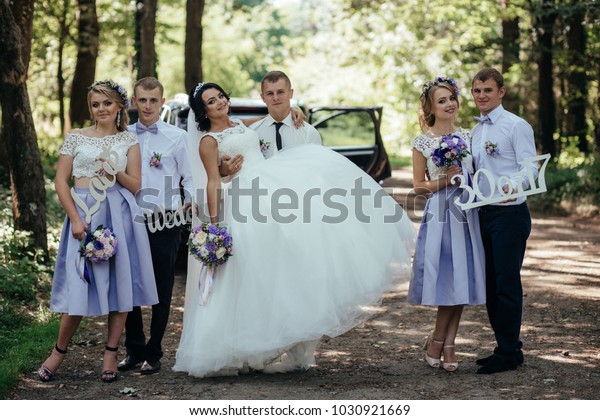 Bride and their friends in violet dresses pose\
in the forest full of\
sunlight