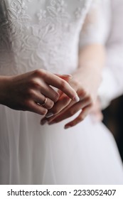 The bride touches the ring with her fingers. Hands in a white wedding dress with a gold wedding ring close-up. - Shutterstock ID 2233052407