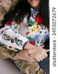 Bride In Ukrainian national embroidered shirt and groom in military uniform hold each other by the hands. Closeup. Concept of marriages during war. War in Ukraine.