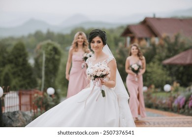 A bride is walking down a path with her bridesmaids. She is wearing a white dress and holding a bouquet of flowers. The scene is set in a garden, with a house in the background