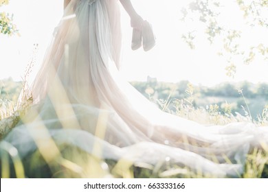 Bride in a wedding dress holds shoes against the sun. fine art photography