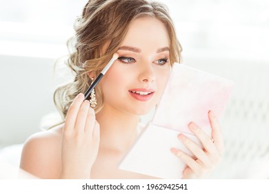 Bride Wedding Makeup. Bridal Make Up. Beautiful Woman Looking At Hand Mirror And Putting Eye Shadow Eyebrow Self Make Up In White Room