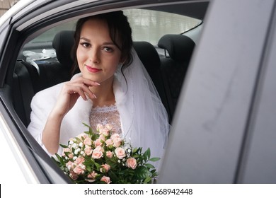 bride in a white dress of Slavic appearance and dark hair sits in a car and looks out the window