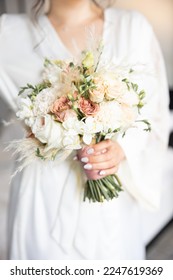 Bride in a white robe holds  wedding bouquet of peonies close up - Shutterstock ID 2247619369