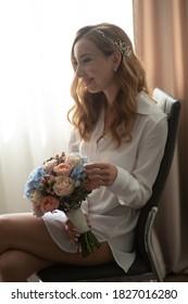 A bride in a white shirt holds a wedding bouquet in her hands. - Shutterstock ID 1827016280
