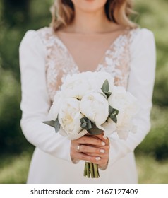 The bride in a white wedding dress is holding a bouquet of white flowers - peonies.. Wedding. Bride and groom. Wedding Dress