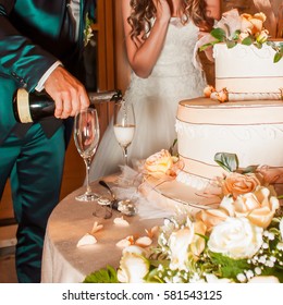 Bridegroom pouring champagne in glasses near a wedding cake. - Shutterstock ID 581543125
