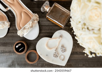 Bride's accessories close-up. Beautiful white shoes, two wedding rings in wooden jewelry box, jewelry, pearl bracelet, perfume and bouquet on wooden background. Bride's accessories on the wedding day - Powered by Shutterstock