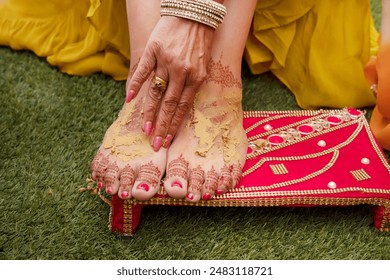 Bride's feet adorned with intricate henna or mehndi designs being covered in turmeric paste as part of the Haldi ceremony at a traditional Indian wedding, Hindu ritual of great cultural significance - Powered by Shutterstock