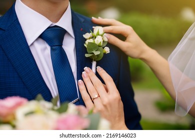 Brides hands putting the boutonniere flower roses on a groom suit. Bride adjusting beautiful groom's boutonniere. Bride puts a buttonhole on a grooms suit. High quality photo