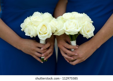 bridesmaids in blue dresses holding a white rose wedding bouquet