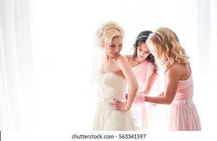 Bridesmaids button up bride's dress while she smiles tender