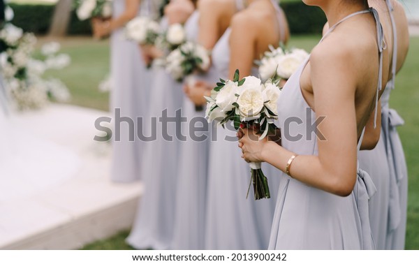 Bridesmaids in dresses stand with bouquets of flowers\
in a row
