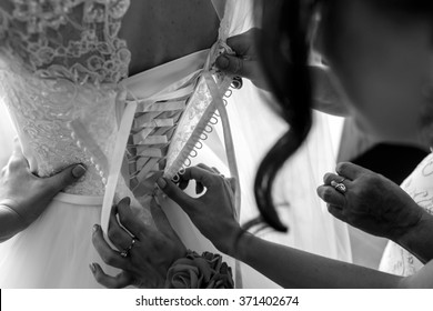 Bridesmaids help put on & tie corset on wedding dress closeup b&w