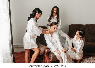 The bridesmaids look at the smiling bride. The bride and her fun friends are celebrating a bachelorette party in matching dresses. Bride and friends in the room - Powered by Shutterstock