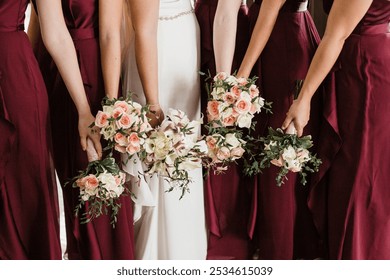 Bridesmaids in maroon dresses holding elegant flower bouquets, captured in a wedding setting showcasing beautiful floral arrangements and bridal fashion.