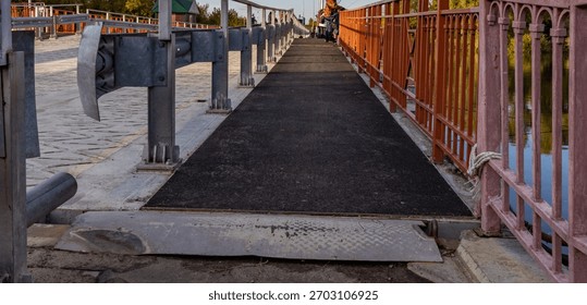Bridge with a black surface and a metal railing. The railing is red and has a few holes in it