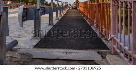 Bridge with a black surface and a metal railing. The railing is red and has a few holes in it