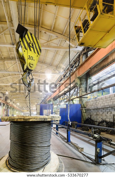 The bridge crane lifts a coil with a steel\
rope. Industrial\
background.