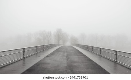 Bridge to fogland. Bridge over a river disappearing in a dense fog - low visibility on November morning. Symmetric vanishing point view of the empty bridge. - Powered by Shutterstock