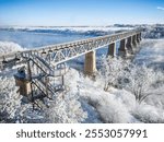 A bridge over a river with snow on it. The bridge is very long and has a staircase on it