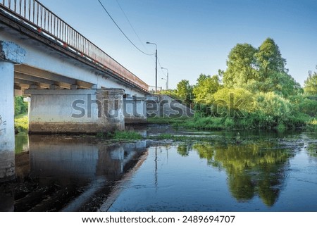 A bridge over a river with a train in the background. The bridge is old and has graffiti on it