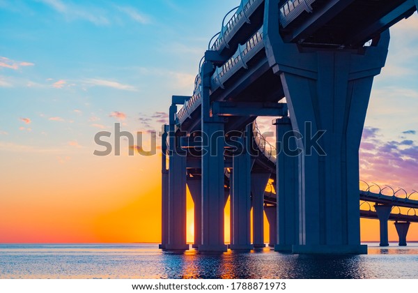 The bridge over the water and colorful\
sky. Sunset and road bridge. Transport infrastructure. The end of\
the day. The highway passes over a\
bridge.