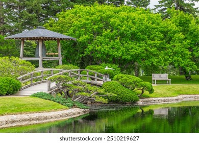 A bridge over a water feature in front of a large bronze bell in the Nikka Yuko Japanese Garden - Powered by Shutterstock