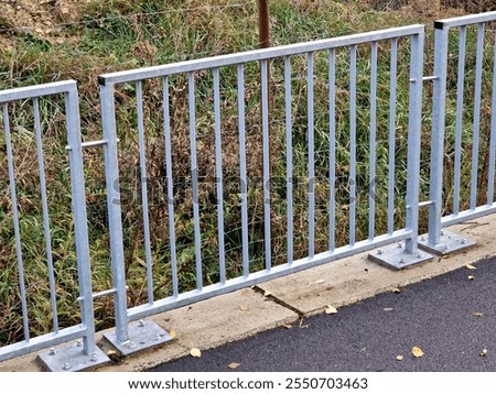  bridge railing with vertical fence posts anchored into the ground with four concrete screws. the railing is fixed from the side of the bridge into the concrete.