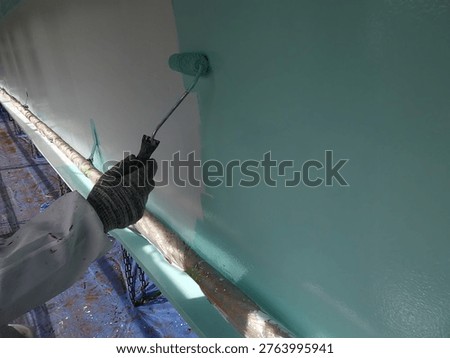 Bridge restoration: Construction worker applying topcoat paint to a steel beam