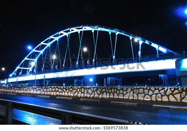 \
bridge with road illuminated\
in the night flashing lights overpass fencing reflection on the\
asphalt