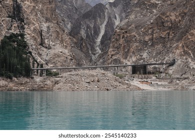 A bridge spans across turquoise waters amid towering rocky cliffs, highlighting a blend of rugged natural beauty and human engineering in a remote, scenic gorge. - Powered by Shutterstock