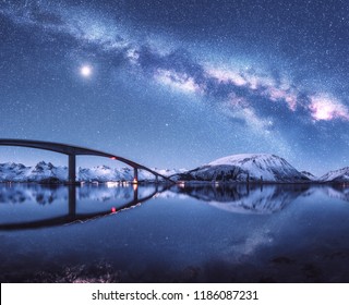 Bridge and starry sky with Milky Way over snow covered mountains reflected in water. Night landscape with road, snowy rocks, sky with moon, milky way, stars, sea. Winter in Lofoten islands, Norway - Powered by Shutterstock