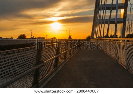 Bridge at sunset, walkway and railing frame the orange sky and horizon, metal structure glows in warm light