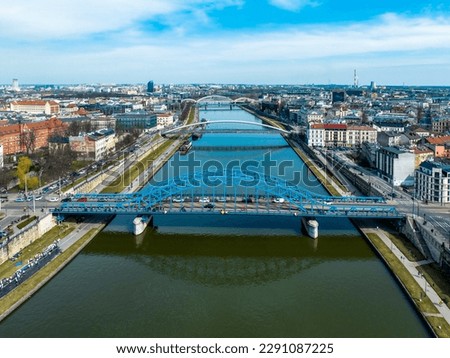 Bridges on Vistula River in Krakow, Poland. Aerial view. Boulevards with waking people. Blue tied-arc bridge in front. Footbridge for pedestrians and cyclist. Far view of new double railway bridge