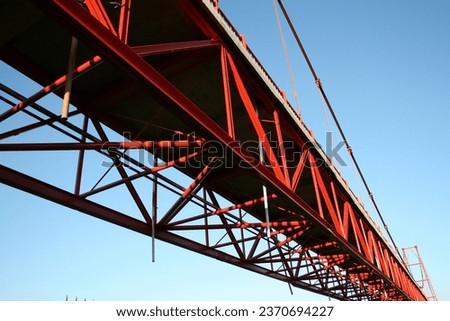 The bridge's undersides, painted red, stretch across the horizon, contrasting the vibrant blue sky, creating a captivating architectural view.