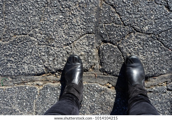 Bridging the Divide - Feet\
of woman in black boots stands with feet across big repair in\
cracked asphalt