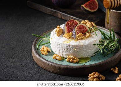 Brie or camembert cheese with figs, walnuts, honey and rosemary on dark background. Low key. French appetizer dessert. Low key