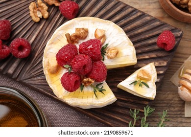 Brie cheese served with raspberries, walnuts and honey on wooden table, flat lay