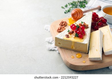 Brie cheese served with red currants, walnuts and honey on light table. Space for text