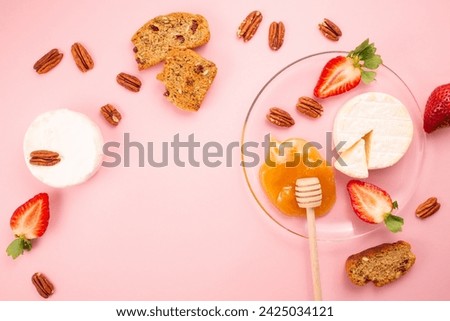 Brie cheese with strawberries, pecans nuts, crackers and honey on pink background. Flat lay. Copy space