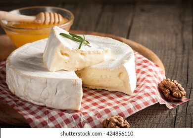 Brie type of cheese. Camembert cheese. Fresh Brie cheese and a slice on a wooden board with nuts, honey and leaves. Italian, French cheese.
