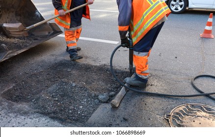 a brigade of servants for road maintenance removes the old asphalt with a jackhammer and shovels into the excavator cart in road construction - Shutterstock ID 1066898669