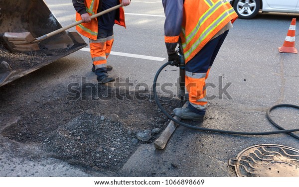 a brigade of servants for road maintenance\
removes the old asphalt with a jackhammer and shovels into the\
excavator cart in road\
construction