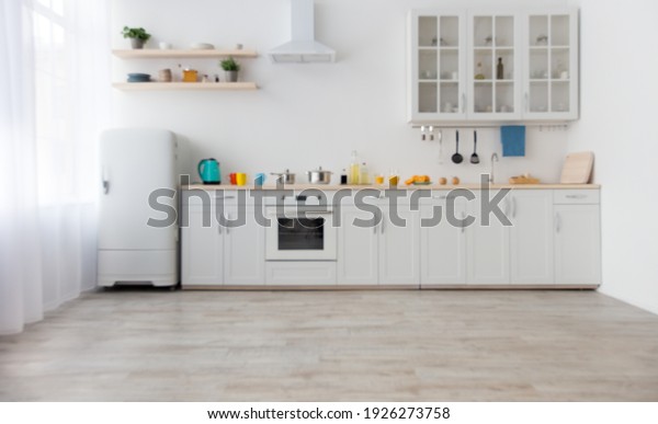 Bright accessories and modern style of kitchen\
interior. White furniture with utensils, colored cups and kettle,\
shelves with dishes and plants in a pots, refrigerator in dining\
room, empty space