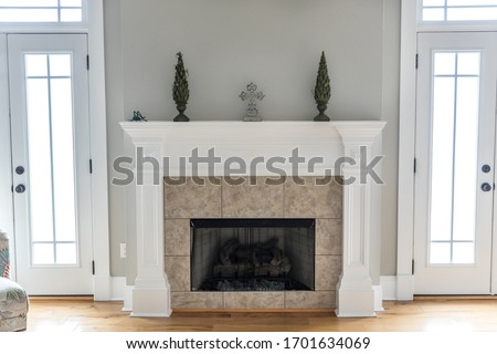 a bright and airy neutral beige gray living room den in a new construction house with a white and tiled fireplace as the main focal point as well as a decorative rug and lots of natural window light.
