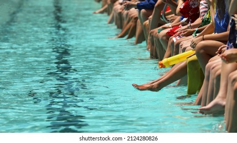 A Bright Aqua Blue Swimming Pool With Students Sitting Dangling Their Feet And Toes In The Water Spectating. High School Swimming Carnival Or Club Race Meeting. 