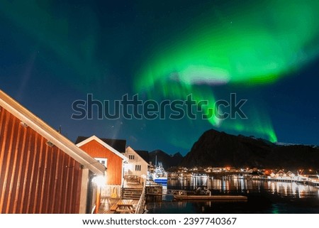 bright aurora borealis over a small coastal Sørvågen village on lofoten islands in norway with mountains on background