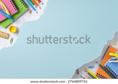 Bright back to school flat lay showing colorful notebook, pencil, scissors, ruler and paperclip arranged around torn blue paper background for education, study, planning and classroom design